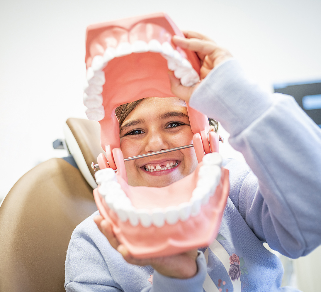 Kind schaut lachend durch ein grosses Zahnmodell — Smile Club, die Zahnarztpraxis fuer Kinder