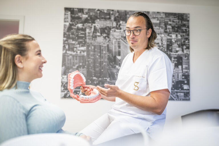 Zahnarzt erklärt einer Patientin die Zahnfleischpflege am Kiefermodell
